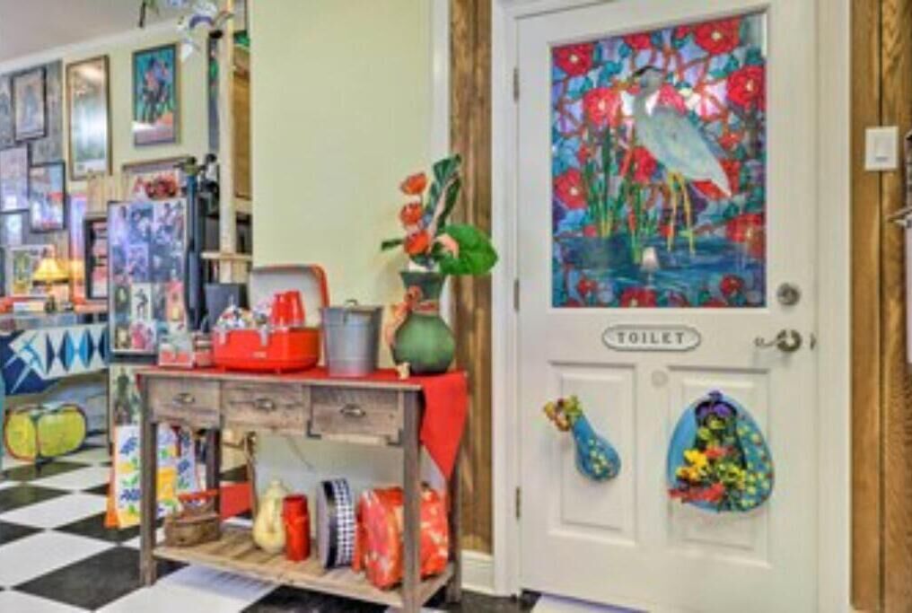 A room with a checkered floor, a painting of a bird and flowers on the door, and a shelf with various items.