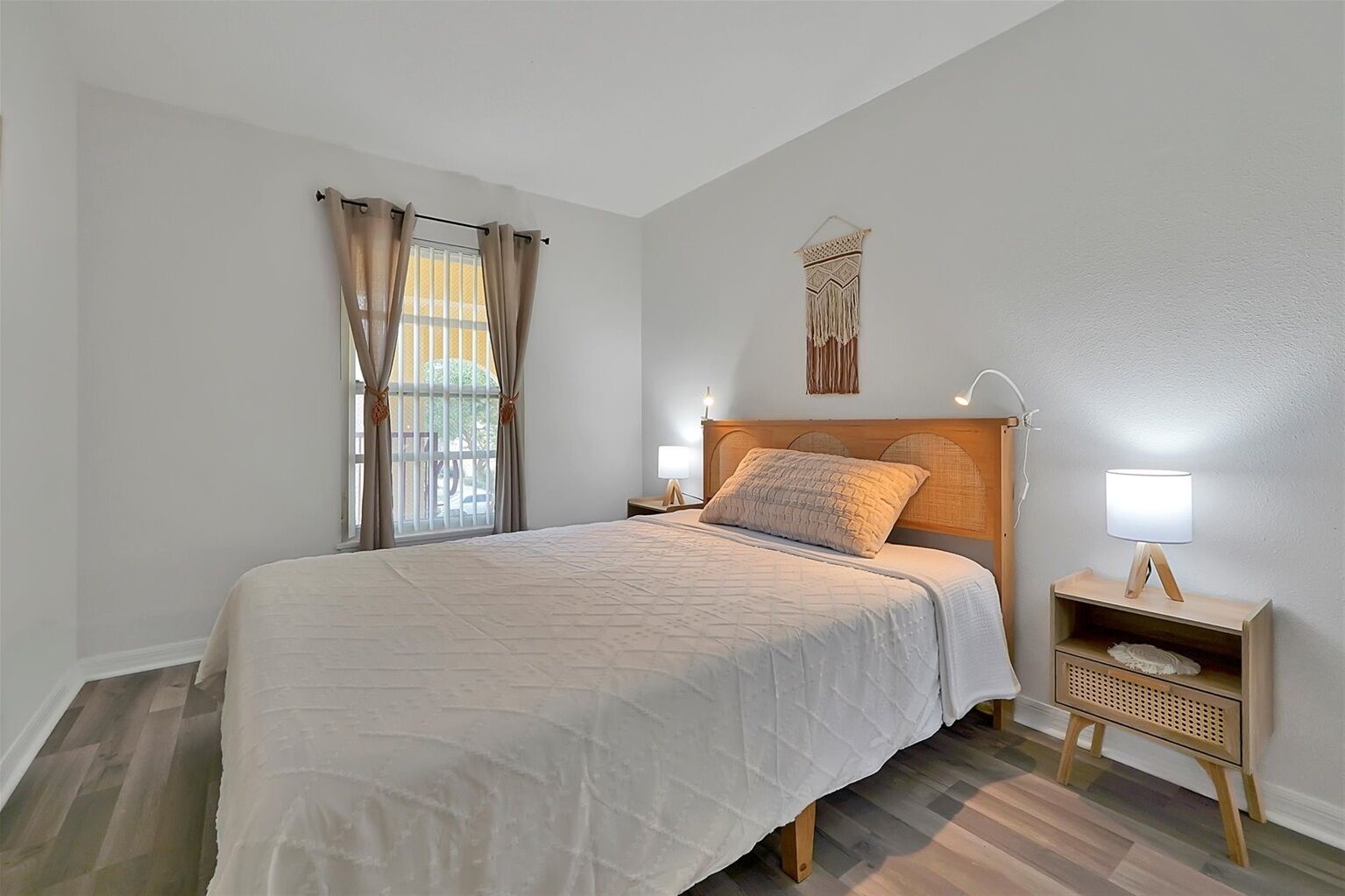 A bedroom with a bed, curtains, a bedside table with a lamp, and a wall-mounted decorative piece.