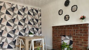 Ein Wohnzimmer mit Wand im geometrischen Muster, einem Kamin aus Ziegelsteinen und einem runden Tisch mit weißer Marmorplatte.
