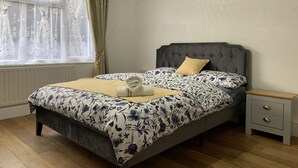 Ein Schlafzimmer mit Bett, Nachttisch, Fenster mit Vorhängen und Heizkörper.