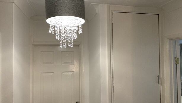Ein Flur mit einer weißen Tür, einem Kronleuchter und einer strukturierten Decke.