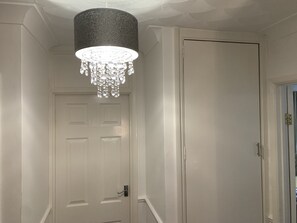 En gang med en hvid dør, en lysekrone og et struktureret loft.