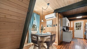 A wooden interior with a round dining table, two chairs, a hanging light fixture, and a kitchen area with a 'WELCOME' sign. - Fox Den~Perfect Escape for Birders (Dauphin Island)