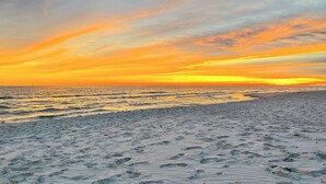 A beach with footprints leading to the water, a clear sky, and a sunset. - Fox Den~Perfect Escape for Birders (Dauphin Island)