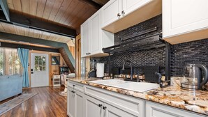 A kitchen with white cabinets, a black backsplash, and a granite countertop. - Fox Den~Perfect Escape for Birders (Dauphin Island)