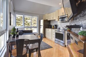 A modern kitchen with a dining area, large windows, and a stone accent wall.