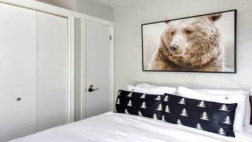 A bedroom with a white bed, a black and white patterned pillow, a framed bear picture on the wall, and a white wardrobe.