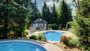 A pool area with two pools, a small building, and surrounding trees.