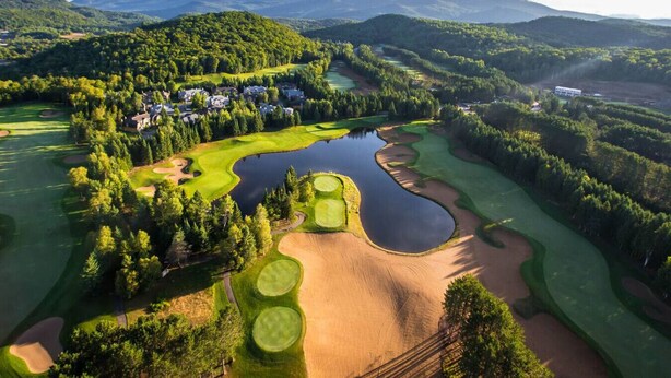 A golf course with a lake, surrounded by forested hills and residential buildings.