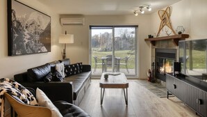 A modern living room with a sofa, a coffee table, a fireplace, and a large window offering a view of the outdoors.