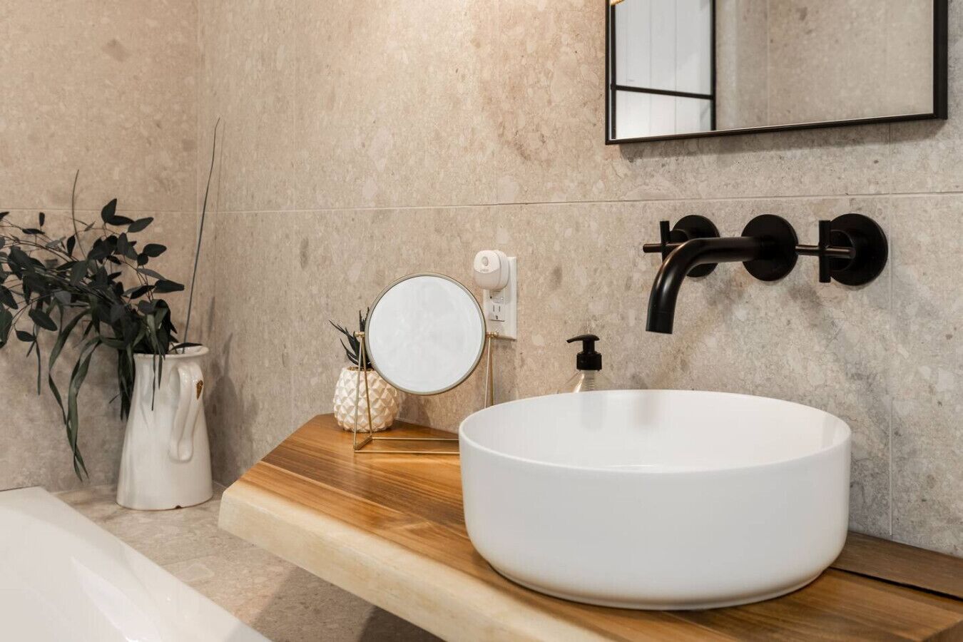 Une salle de bain moderne avec un grand lavabo blanc, un robinet noir, un miroir rond et un plan de toilette en bois.