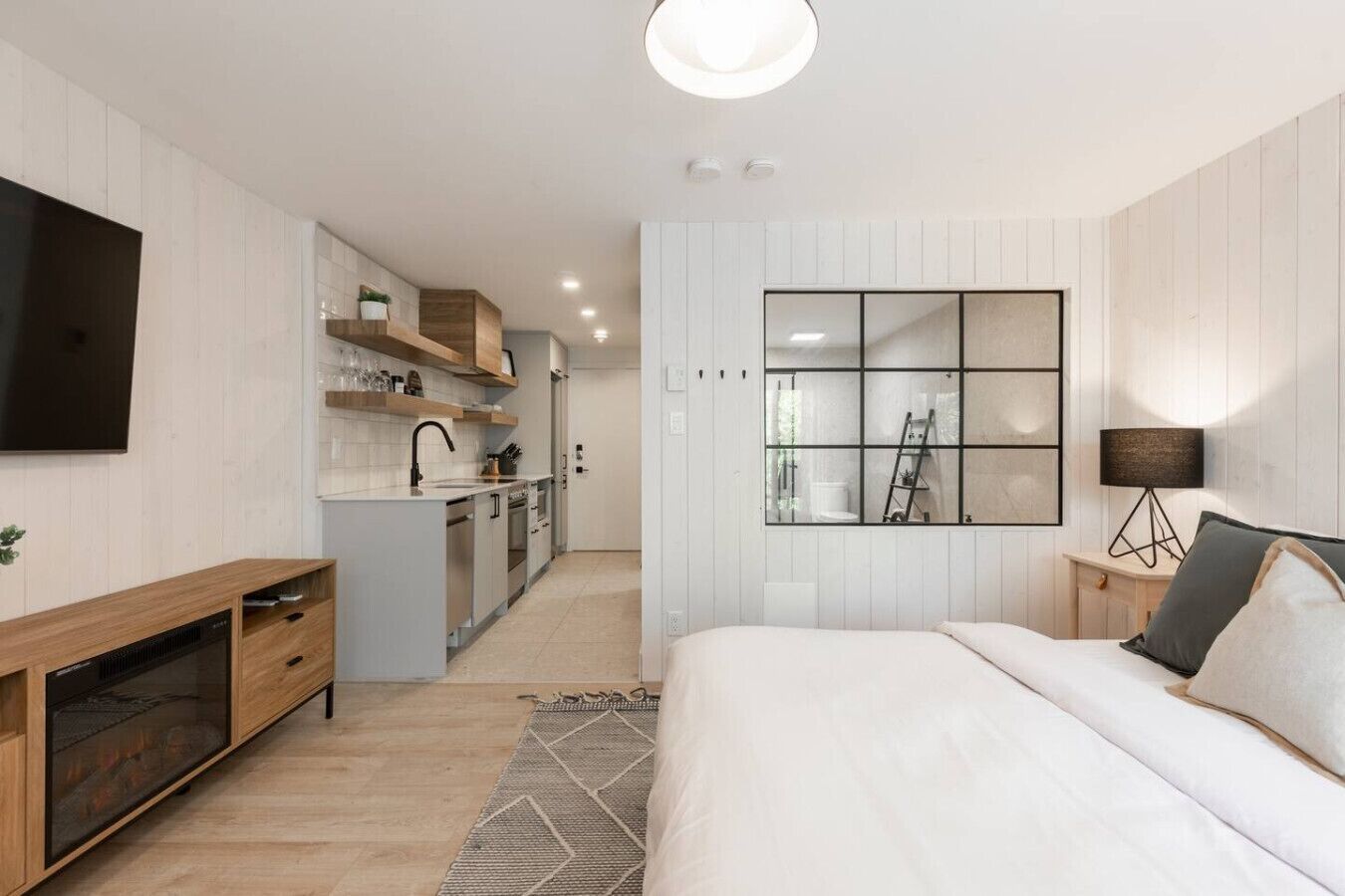 Une chambre moderne avec un grand lit, une télévision, une table de chevet avec une lampe et une vue sur la cuisine.