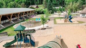 Ein Spielplatz mit Rutschen, einem Wasserspielbereich und überdachten Sitzmöglichkeiten.