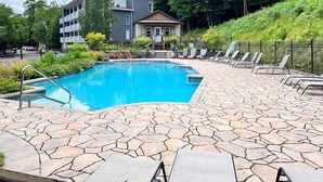Ein Schwimmbecken mit Steinplatten, Liegestühlen und einem Gebäude im Hintergrund.