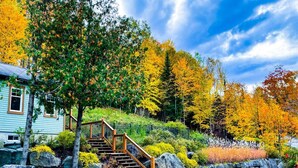 Ein Haus mit einer Holztreppe, die zu einer Terrasse führt, umgeben von Herbstlaub und einer Steinmauer.