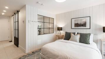 Une chambre à coucher moderne avec un grand lit, une armoire, un miroir et un tableau encadré au mur.