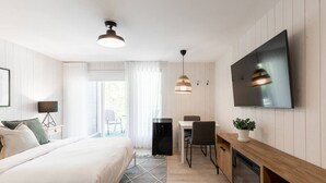 Ein modernes Hotelzimmer mit einem großen Bett, einem Schreibtisch, einem Esstisch und einem an der Wand befestigten Fernseher.