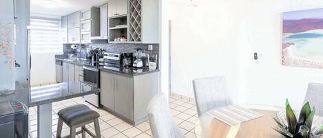 Una cocina moderna con armarios grises, encimera negra y un comedor con mesa redonda y sillas grises.