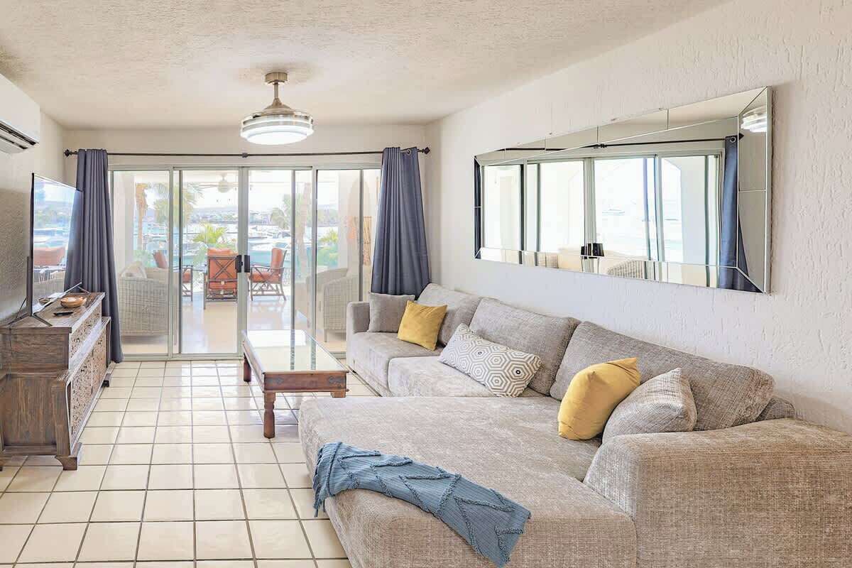 A living room with a sofa, a coffee table, and a TV. There is a sliding glass door leading to an outdoor area with a pool.