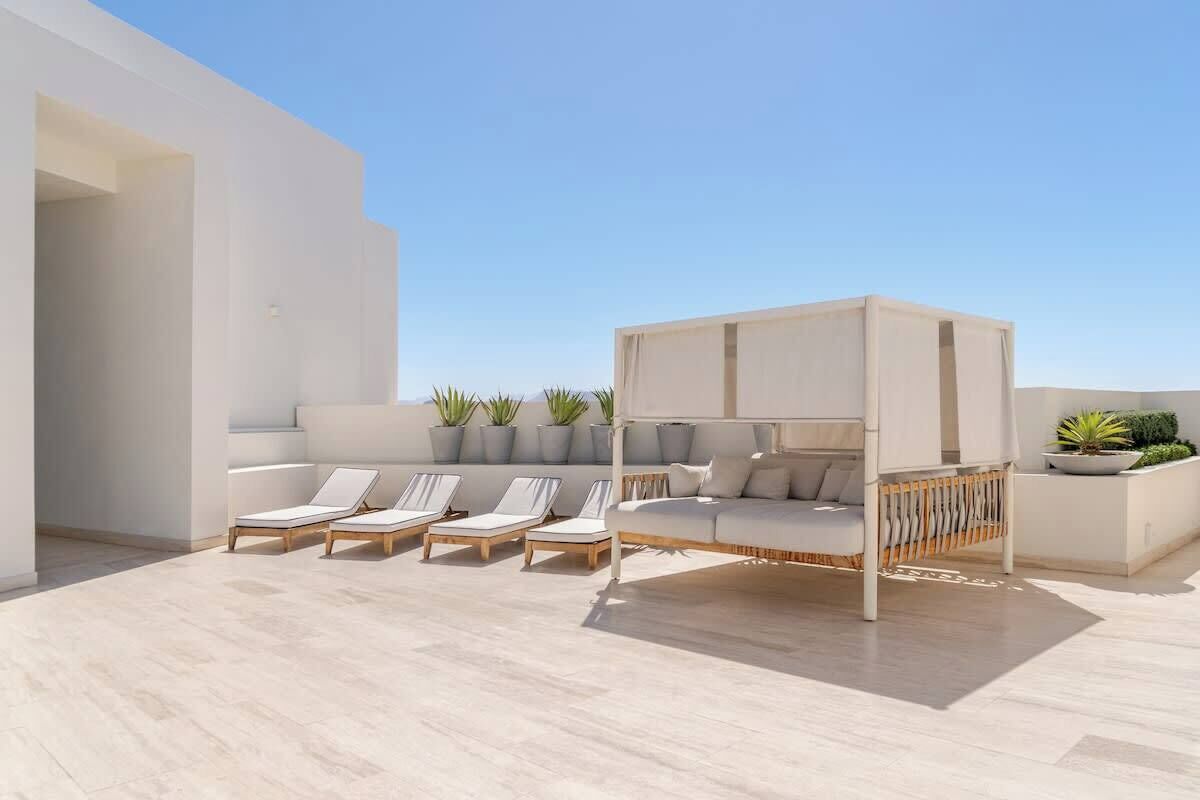 Een terras op het dak met witte banken, lounge fauteuils en plantenpotten.