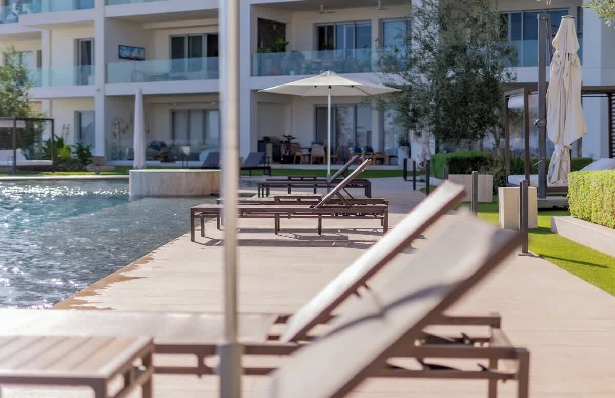 A poolside area with lounge chairs and umbrellas, a clear view of the pool, and a modern building in the background.