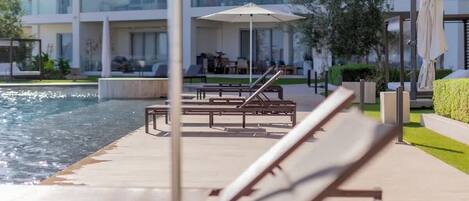 A poolside area with lounge chairs and umbrellas, a clear view of the pool, and a modern building in the background.