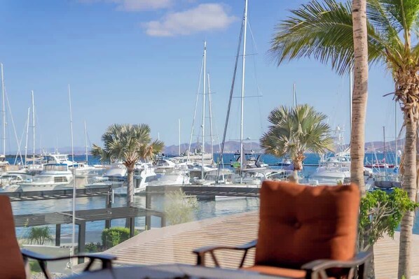 A marina with boats docked, palm trees, and a wooden deck with chairs.
