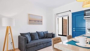 A modern living room with a grey sofa, a small table with a white mug, a floor lamp, and a blue door. - Pineda Complex for Groups up to 16 Guests Downtown (La Paz)