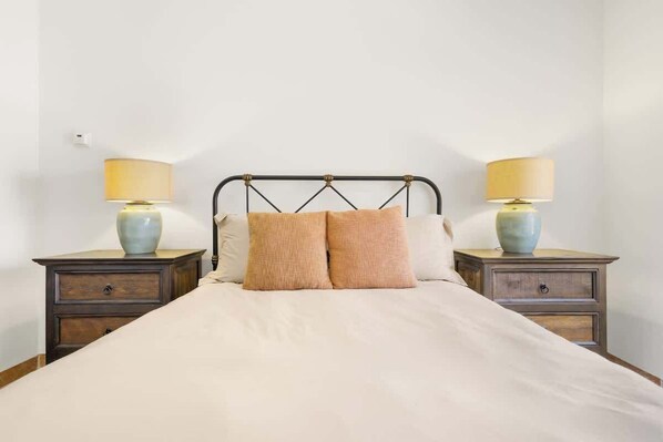 A bed with a metal frame, two bedside tables with lamps, and a plain wall.