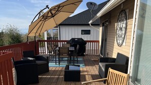 Una terraza de madera con mobiliario exterior, incluyendo sillas y una mesa, y una parrilla.