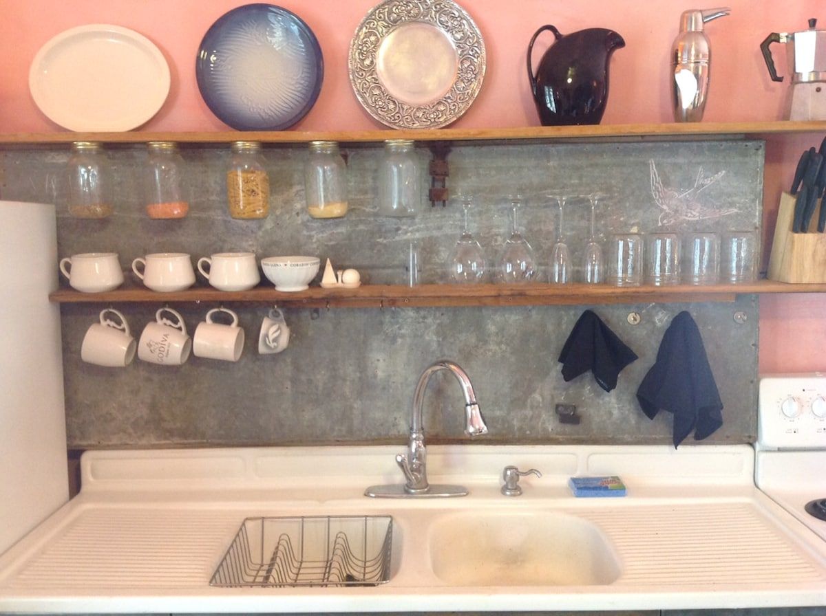 A kitchen with a sink, various dishes, and utensils on shelves.