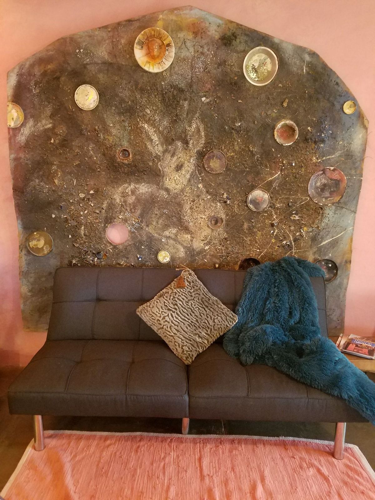 A sofa with a patterned pillow and a blue throw blanket against a textured wall with circular metallic decorations.