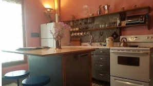 A compact kitchen with a central island, a stove, and a sink. There are stools at the island, and a vase with flowers on the countertop. - Romantic Adobe Casita, Hot tub, Kitchen, Woodstove, astounding views, historic. (Los Cerrillos)