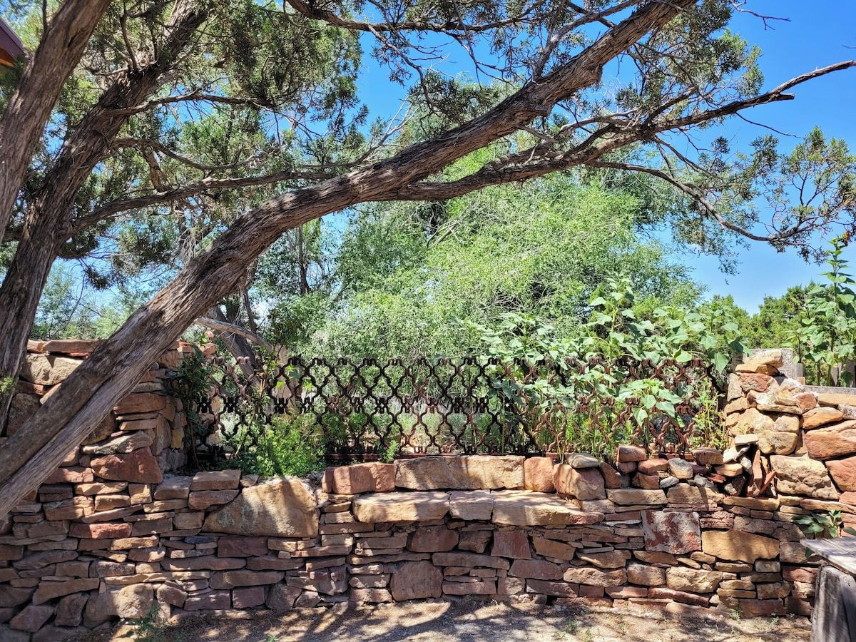 Un muro de piedra con una valla metálica y un árbol.