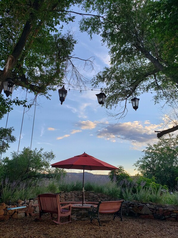 An outdoor seating area with stone walls, a red umbrella, and hanging lanterns. - The Cerrillos Manor Carriage House Hot tub Romance (Los Cerrillos)