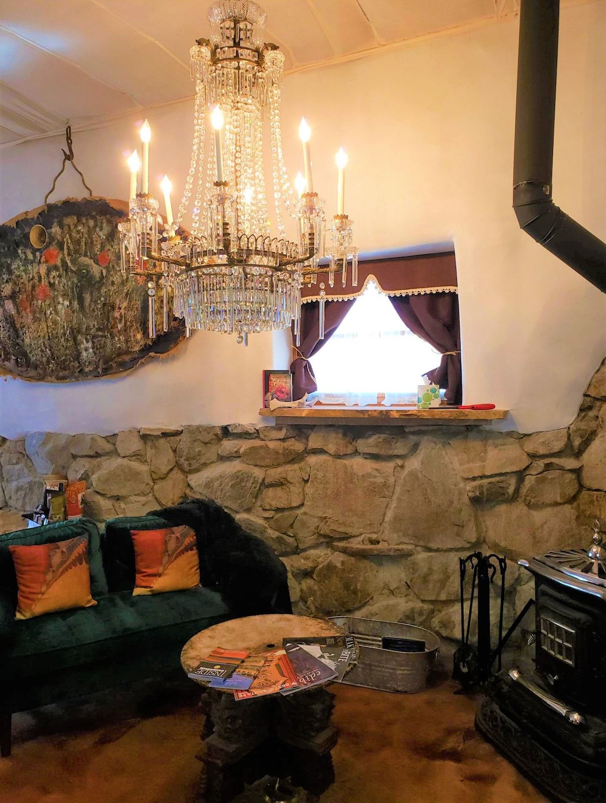 A cozy living room with a stone wall, a chandelier, a fireplace, and a sofa with cushions.