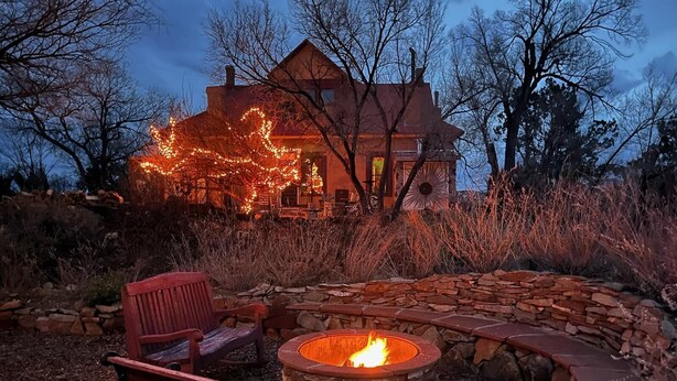 A stone fire pit with a fire, a red chair, and a stone wall. - Romantic, Rock Carriage House, Hot Tub, Woodstove, Kitchen on Historic Property (Los Cerrillos)