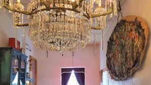 A room with a large chandelier, a stone wall, a green sofa, and a window with curtains. - Romantic, Rock Carriage House, Hot Tub, Woodstove, Kitchen on Historic Property (Los Cerrillos)