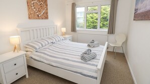 A neatly arranged bedroom with a single bed, bedside tables, a chair, and a window with curtains. - Sea House (Littlehampton)