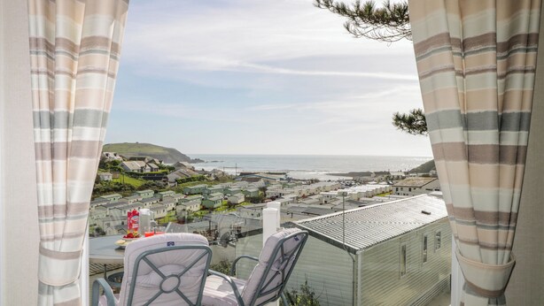 A balcony with a view of a coastal town, a table with chairs, and a bottle of water.
