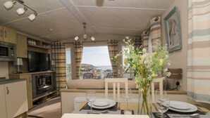 A dining area with a table set for four, a television, and a view of the sea.