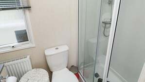 A bathroom with a toilet, a glass-enclosed shower, a radiator, and a wicker basket. - Ocean Pearl (Kingsbridge)
