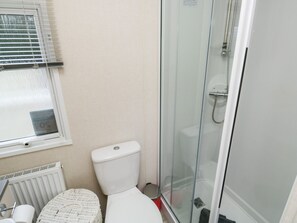 A bathroom with a toilet, a glass-enclosed shower, a radiator, and a wicker basket.