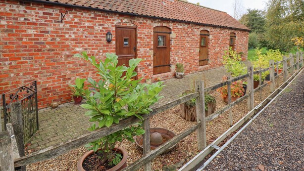 A brick building with a tiled roof, wooden doors, and a garden with potted plants. - Ratty's Retreat (Spilsby)