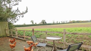 A wooden deck with a table and chairs, surrounded by a fence, overlooking a field. - Ratty's Retreat (Spilsby)