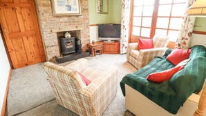 A cozy living room with a fireplace, two plaid sofas, a television, and a large window with curtains. - Ratty's Retreat (Spilsby)