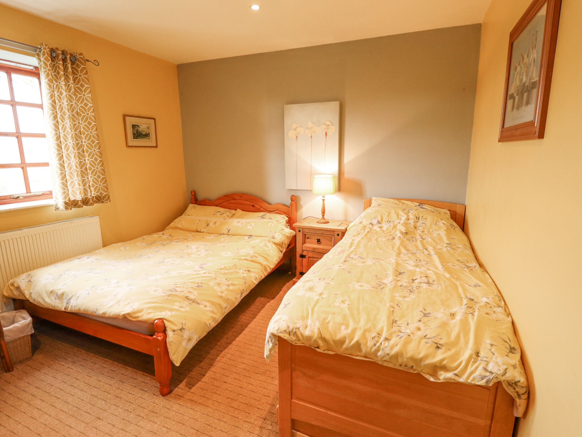 Een slaapkamer met twee eenpersoonsbedden, een nachtkastje met een lamp, een radiator en een raam met gordijnen.