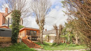 Una casa moderna con una escalera de madera que lleva a una terraza, rodeada de vegetación y árboles.