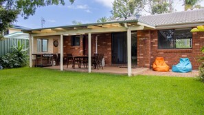 Ein Haus mit überdachter Terrasse, Ziegelaußenwand und Rasenfläche.