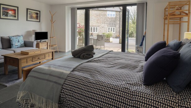 Et moderne soveværelse med en stor seng, en sofa, et fjernsyn og et træsidebord.